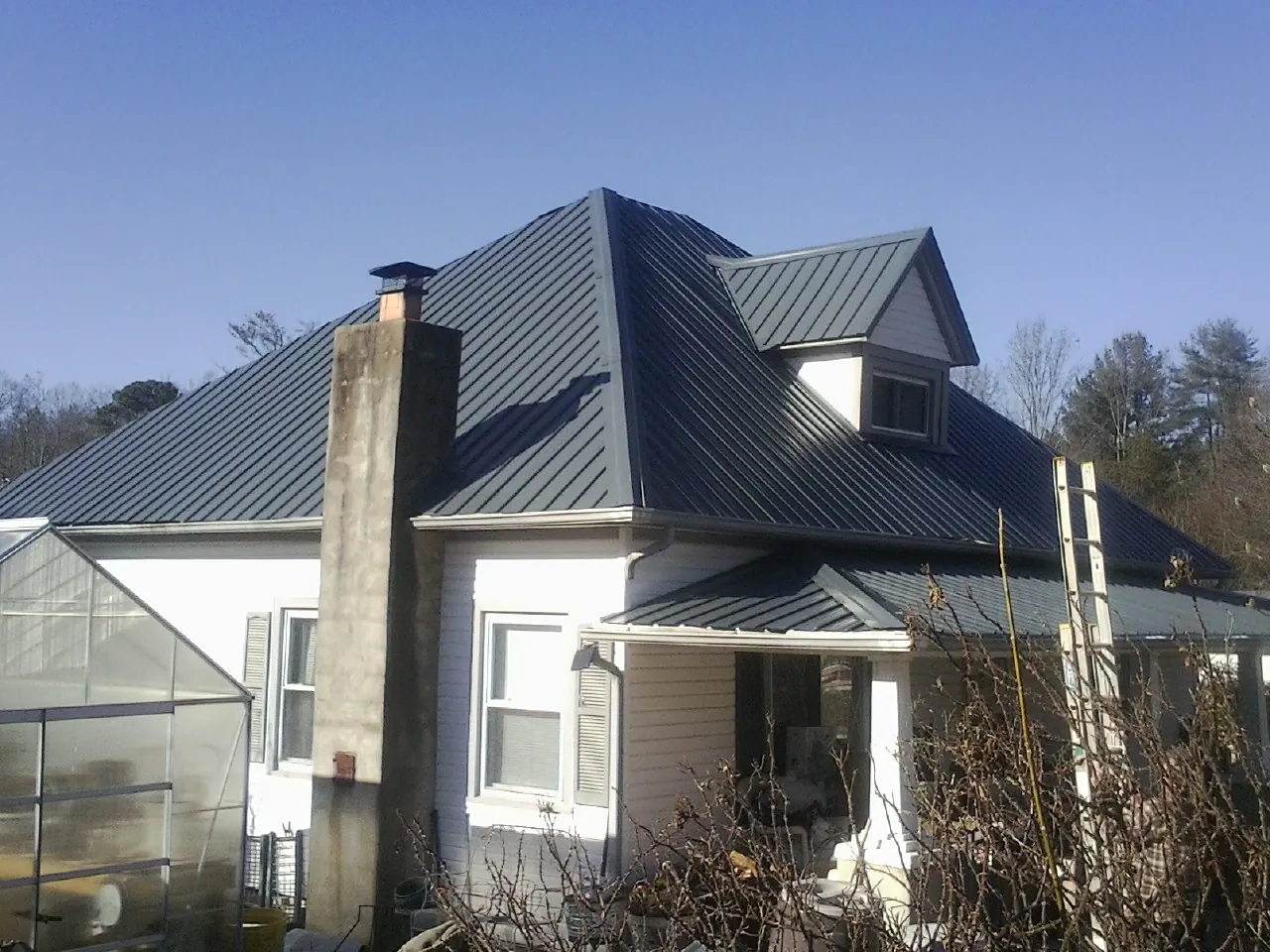 Dark blue standing seam metal roof on a white farmhouse with dormer — Slate & Tile Roof Repair by Roofing Brothers in Huntington